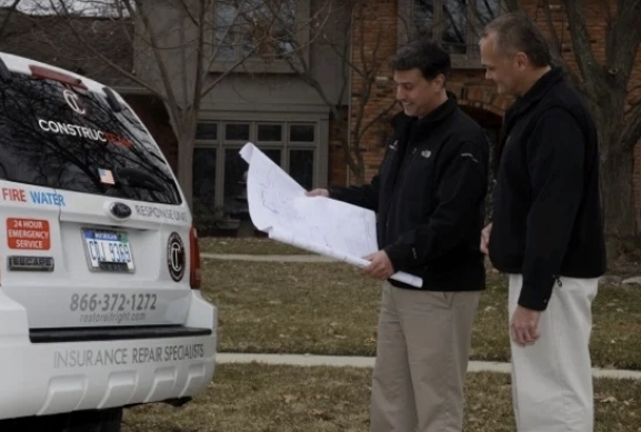 ConstrucTEAM employees reviewing blueprints outside a home near a ConstrucTEAM van